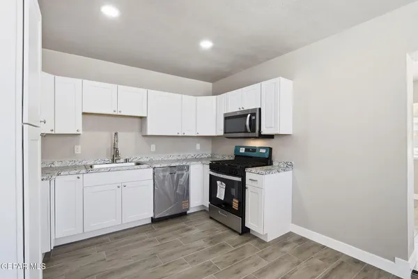 a kitchen with stainless steel appliances granite countertop a stove top oven a sink a refrigerator and white cabinets with wooden floor