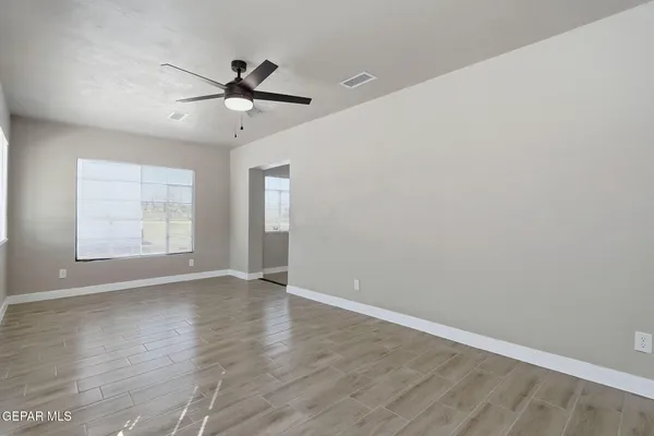 an empty room with wooden floor ceiling fan and windows