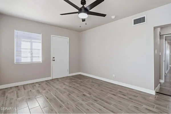 a view of an empty room with wooden floor and a ceiling fan