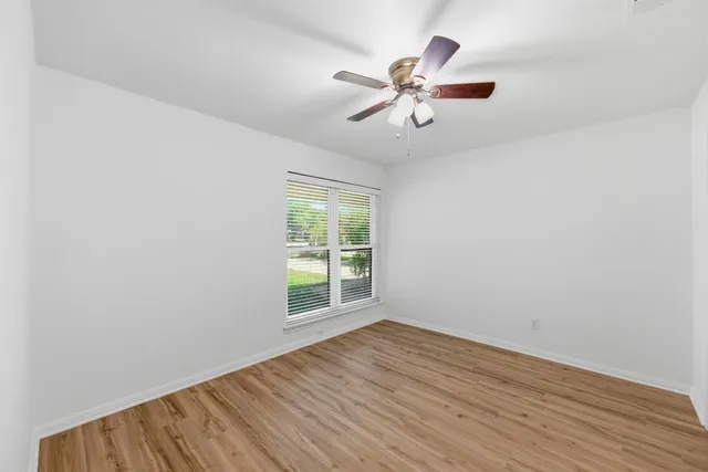 an empty room with wooden floor fan and windows