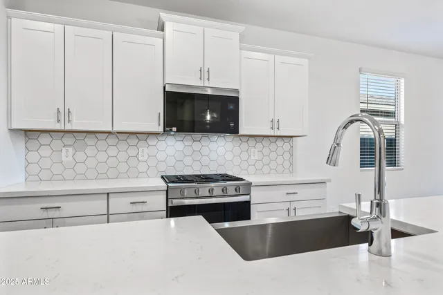 a kitchen with granite countertop a stove a sink and white cabinets