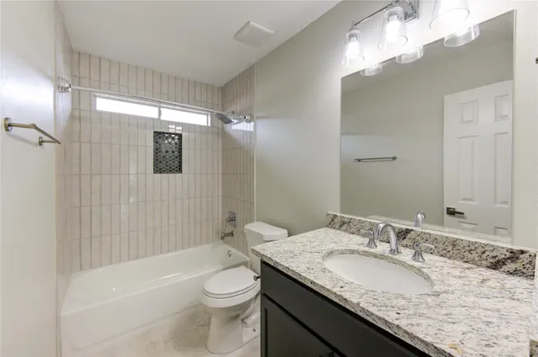 a bathroom with a granite countertop sink a toilet a mirror a bathtub and shower