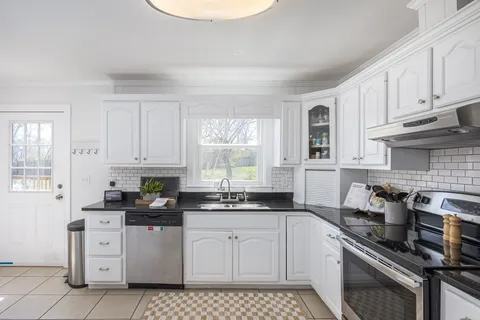 a kitchen with white cabinets appliances a sink and a window