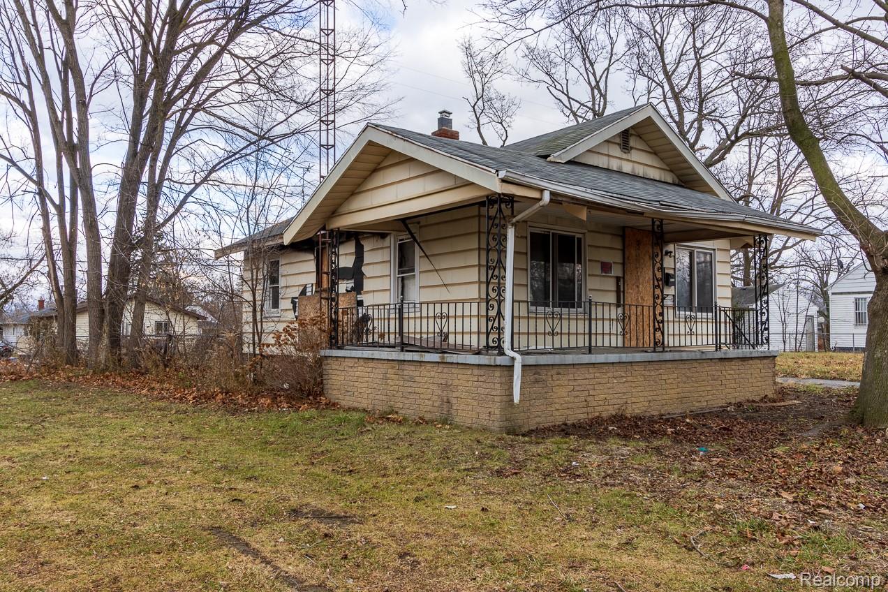 View of side of home with a porch, a chimney, a lawn, and roof with shingles