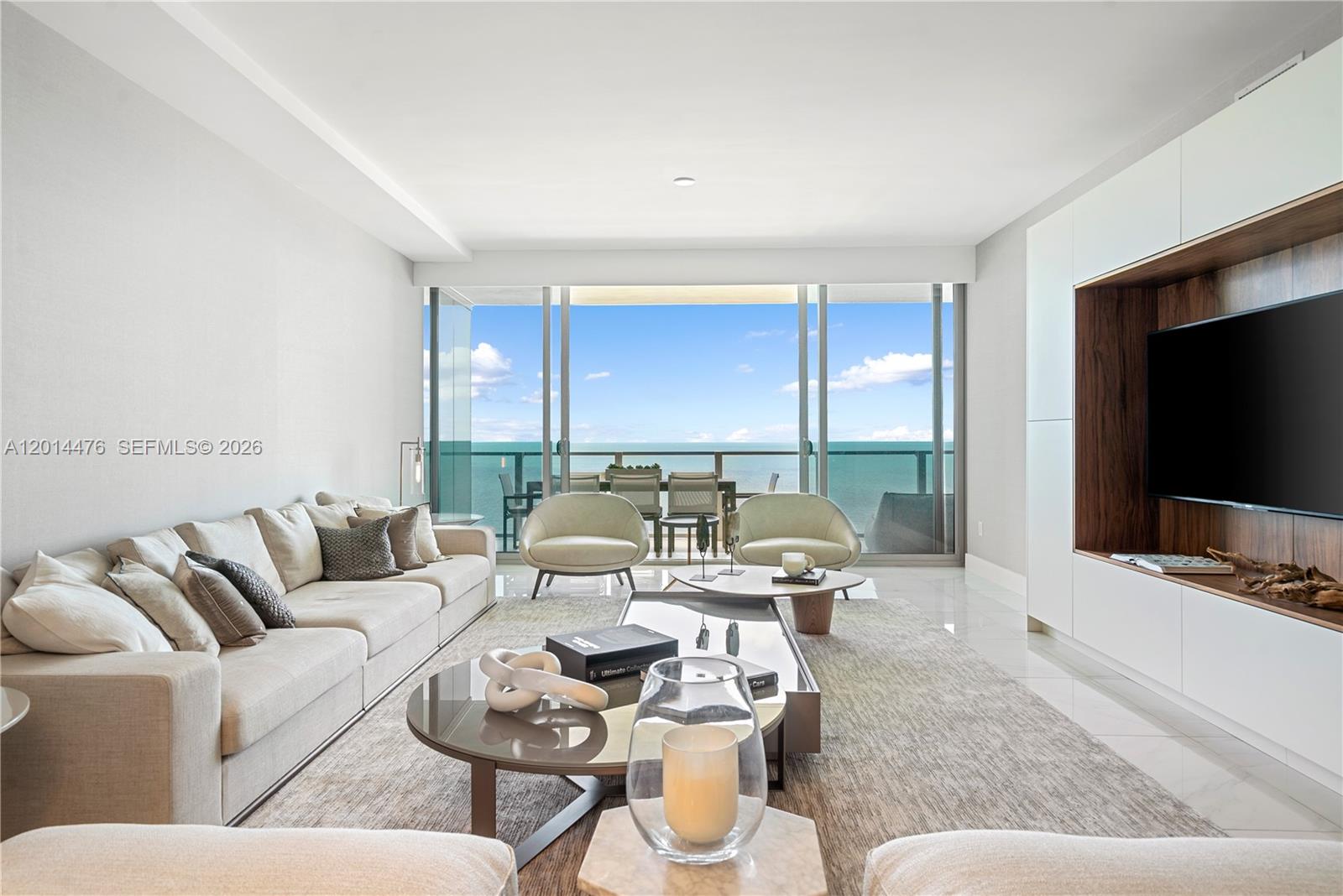 360 Ocean Drive, Unit 1106S Key Biscayne, FL 33149 - Photo 7 of 67 Living Room with Water Views – Expansive glass doors frame bright water views and open to the balcony beyond. The room is designed with a comfortable seating area, custom media wall, and light-toned finishes that complement the coastal backdrop.