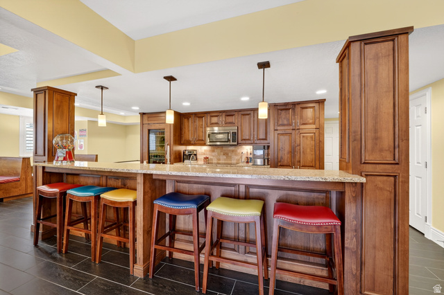 714 Draper Heights Way Draper, UT 84020 - Photo 51 of 88 Kitchen with wood finish cabinets, a kitchen bar, hanging light fixtures, light stone counters, and backsplash
