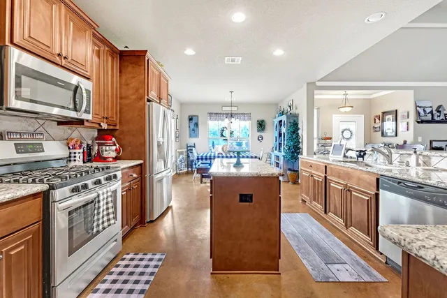 a kitchen with stainless steel appliances granite countertop a stove top oven a sink dishwasher a dining table and chairs with wooden floor