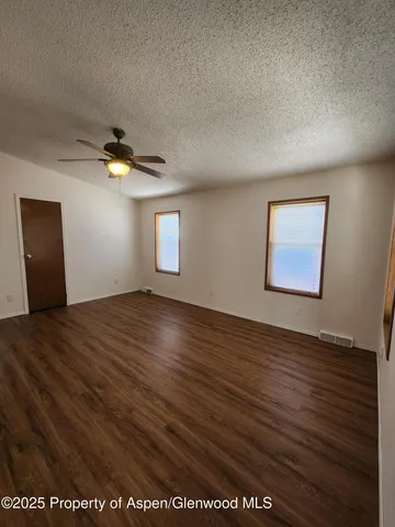 an empty room with wooden floor fan and windows