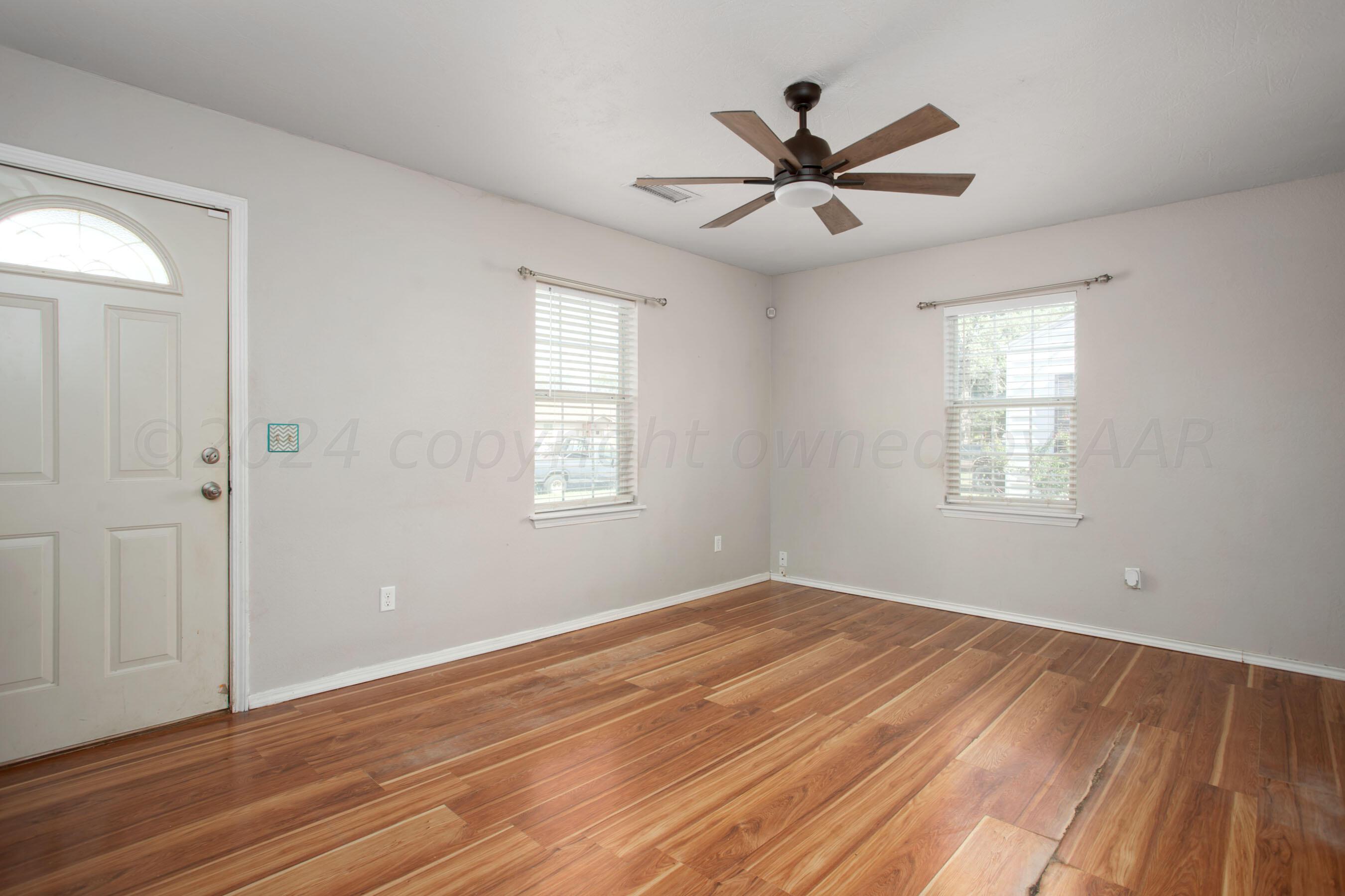 4625 South Travis Street Amarillo, TX 79110 - Photo 3 of 24 an empty room with wooden floor a ceiling fan and windows