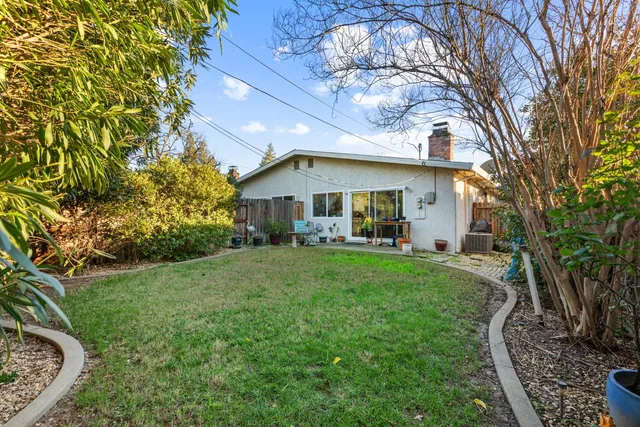 a view of a white house in front of a yard with plants and large trees