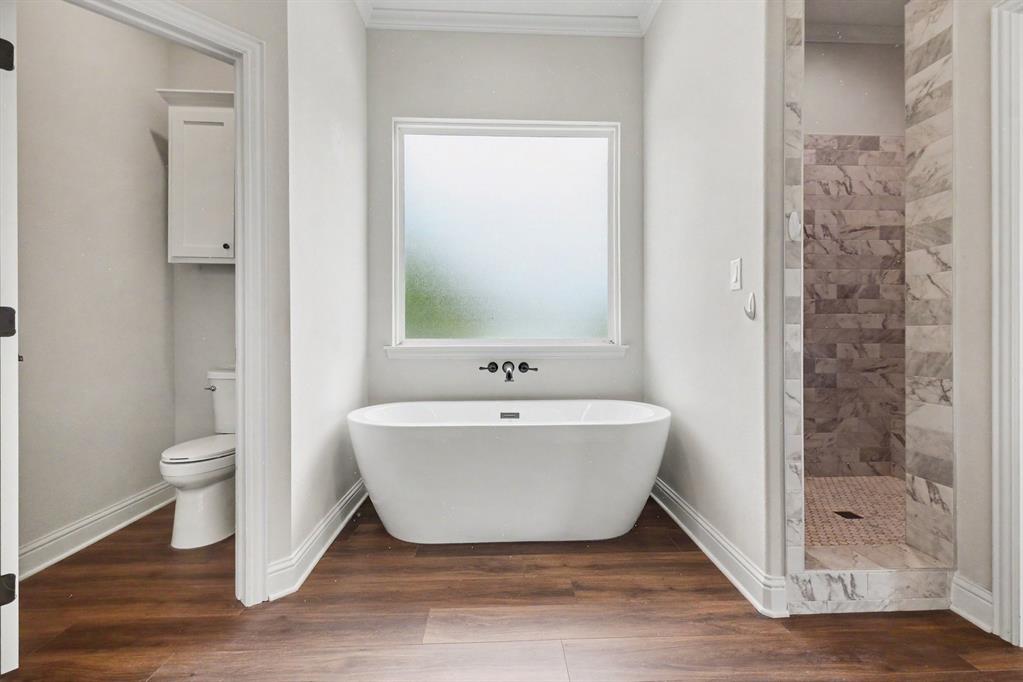 530 P R 491 Leonard, TX 75452 - Photo 19 of 35 Bathroom featuring a freestanding soaking tub with wall-mounted fixtures, a frosted window, a walk-in shower with stone tile, wood-finish flooring, and a separate water closet with built-in cabinetry