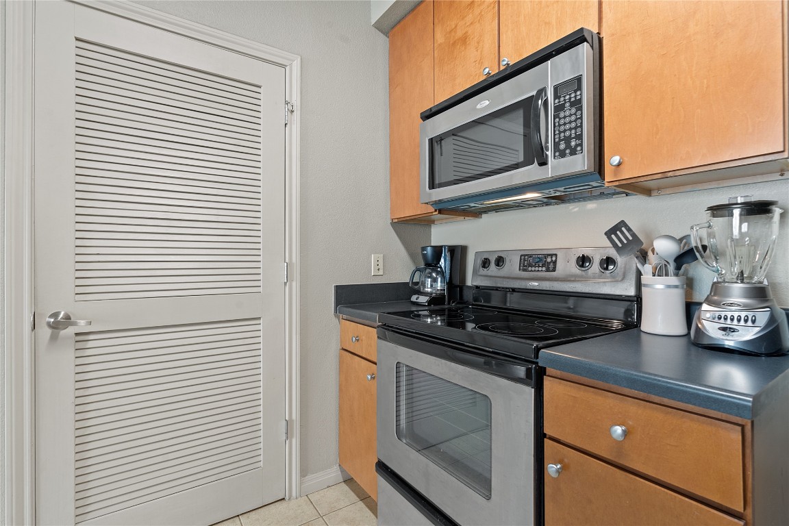 2515 Pearl Street, Unit 315 Austin, TX 78705 - Photo 11 of 17 Kitchen with dark countertops, stainless steel appliances, light tile patterned floors, and brown cabinetry