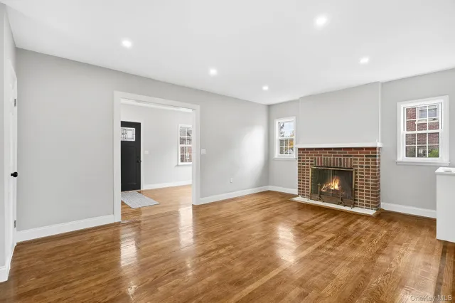 a view of an empty room with wooden floor fireplace and a window
