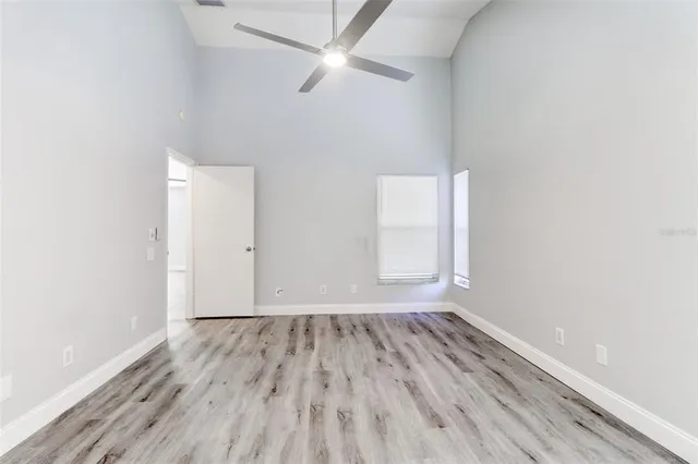 an empty room with wooden floor fan and windows