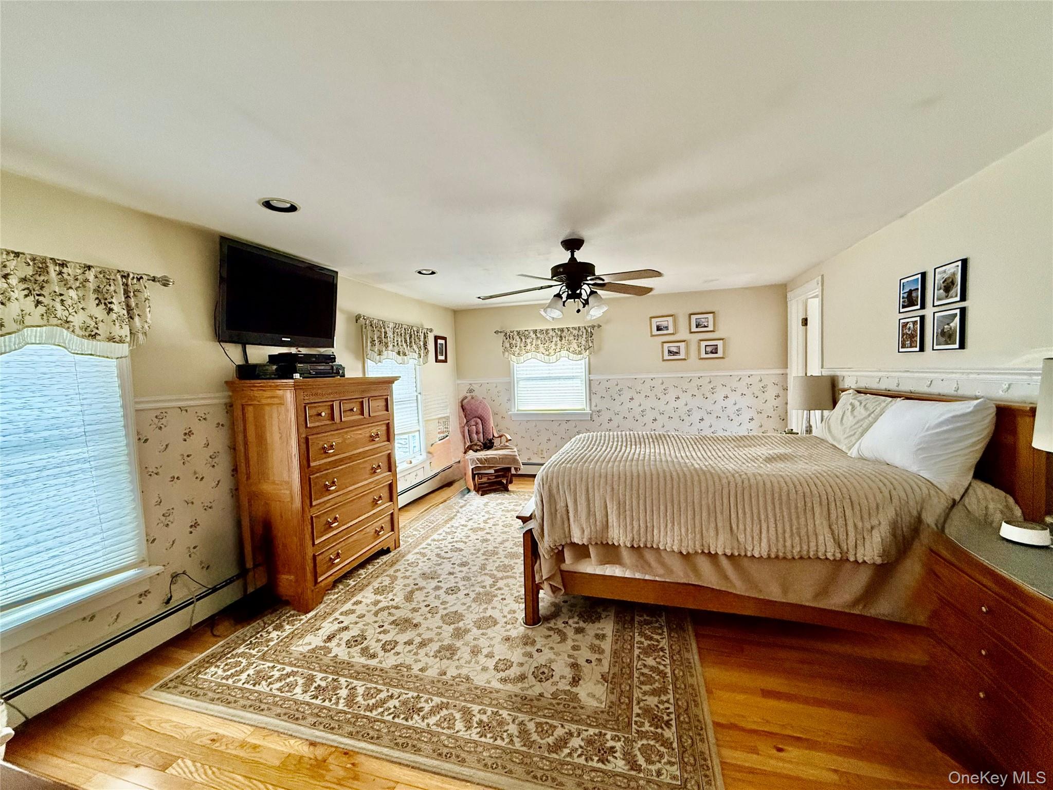 912-918 Hollow Road Salt Point, NY 12578 - Photo 26 of 38 Bedroom featuring a baseboard heating unit, a wainscoted wall, a ceiling fan, light wood-style flooring, and wallpapered walls