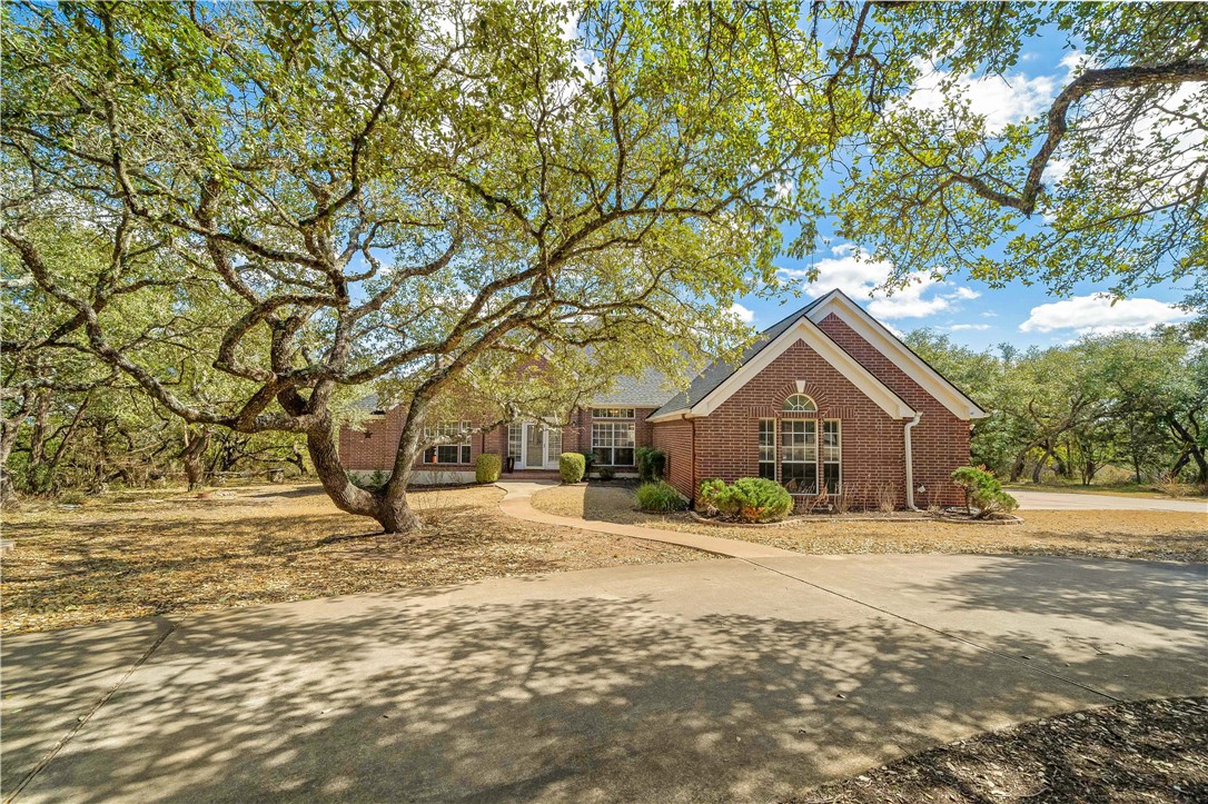 a yellow house in middle of a yard with large trees