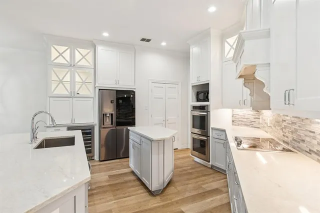 a kitchen with stainless steel appliances kitchen island granite countertop a refrigerator oven a sink dishwasher and white cabinets with wooden floor