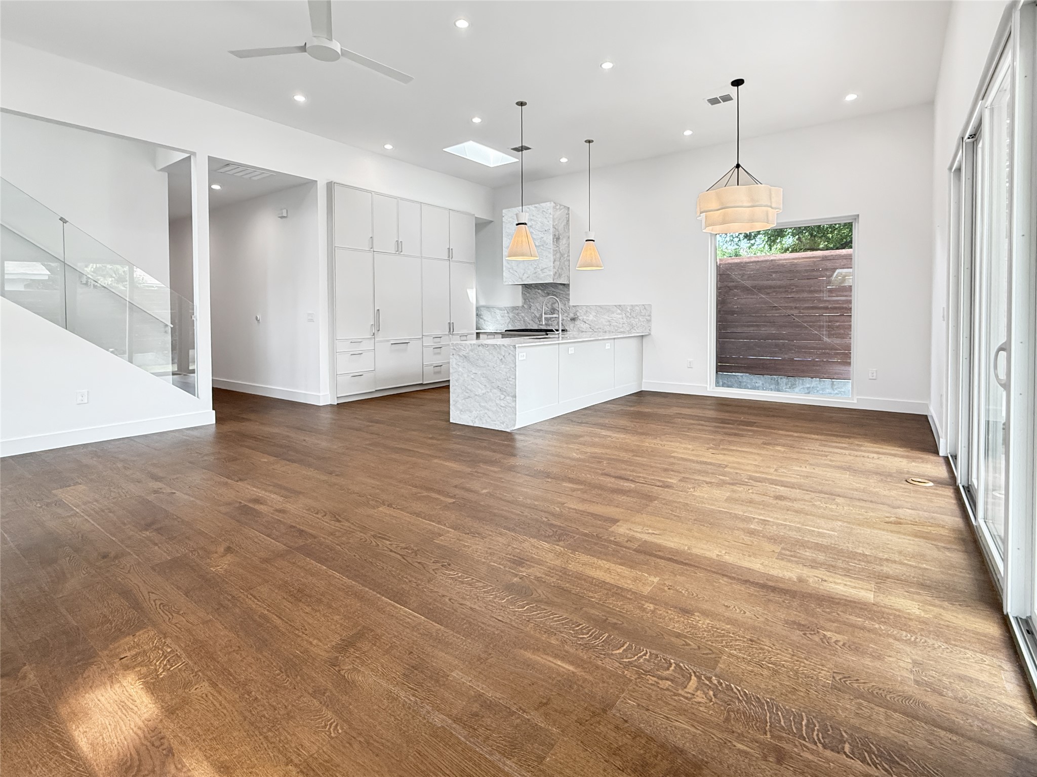 127 Frederick Street Austin, TX 78704 - Photo 12 of 34 Open-concept living space featuring wood-finish flooring, a contemporary kitchen with stone countertops and full-height white cabinetry, and a glass-paneled staircase