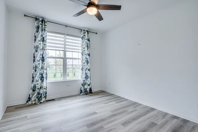 an empty room with wooden floor fan and windows
