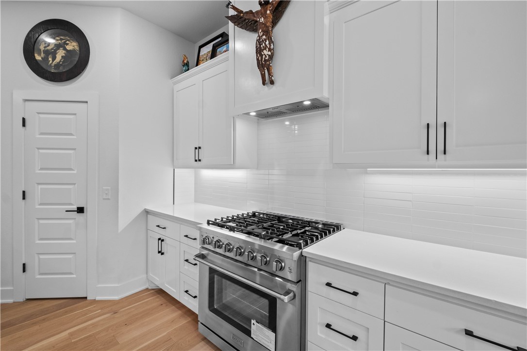 2055 Collins Drive Pea Ridge, AR 72751 - Photo 12 of 53 White shaker cabinetry with matte black hardware, stainless steel range with overhead hood, integrated under-cabinet lighting, light-toned wood-finish flooring, and a white subway tile backsplash