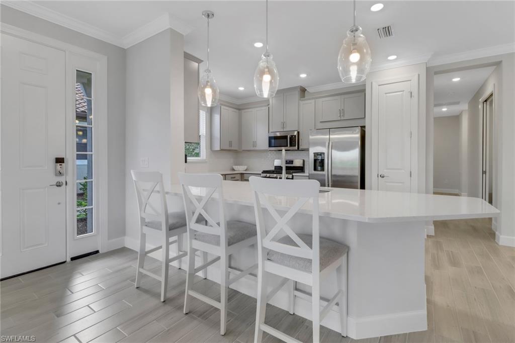 Kitchen with light countertops, gray cabinetry, visible vents, a breakfast bar area, and stainless steel appliances