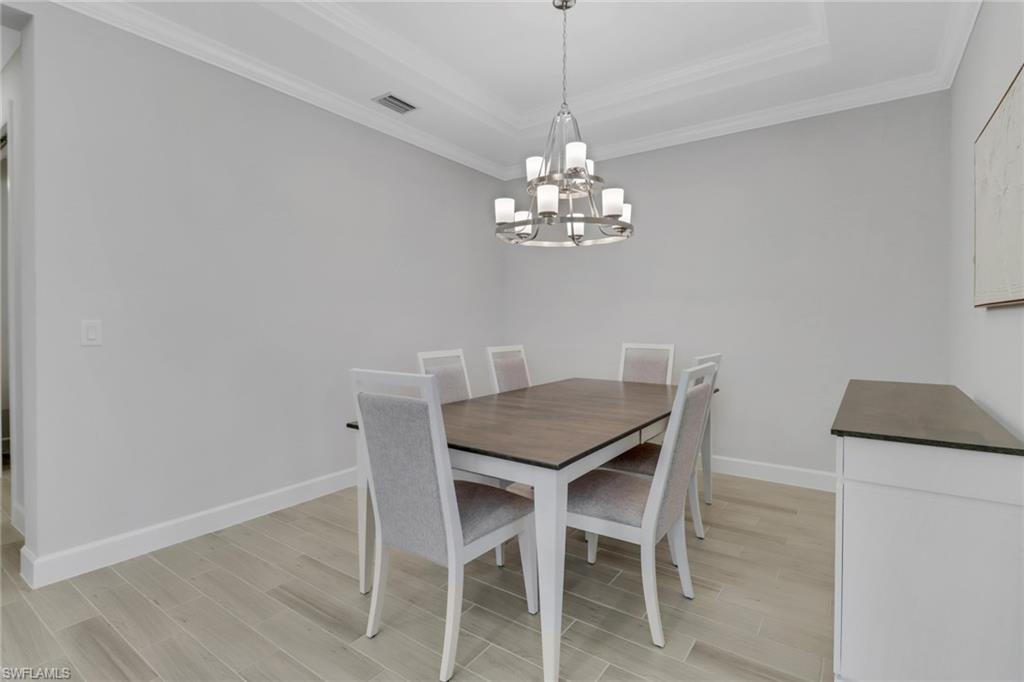 15561 Vittorio Street Naples, FL 34114 - Photo 6 of 16 Dining area with a notable chandelier, light wood-style flooring, crown molding, visible vents, and a raised ceiling