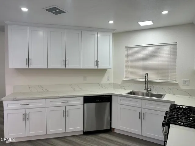 a kitchen with white cabinets white appliances sink and dishwasher with wooden floor