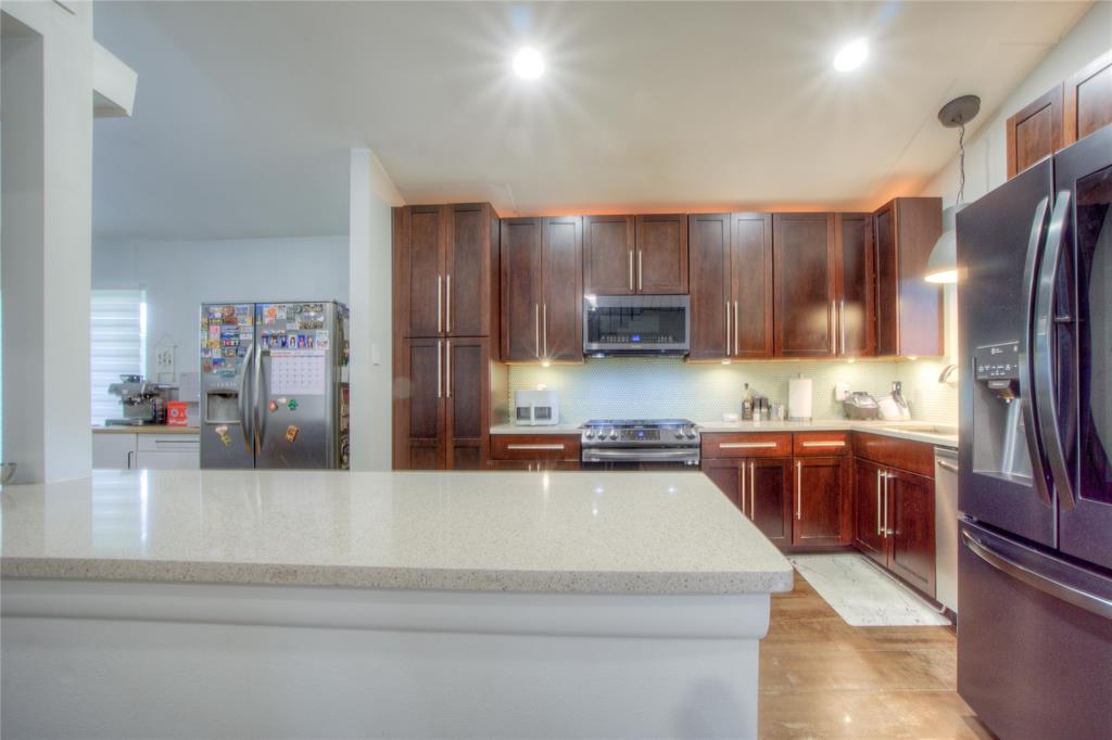 12231 Veronica Road Farmers Branch, TX 75234 - Photo 10 of 26 Spacious kitchen featuring an expansive light-toned countertop, rich wood-finish cabinetry with brushed nickel hardware, and stainless steel appliances