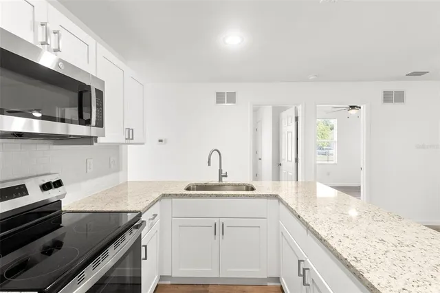 a kitchen with granite countertop a sink stainless steel appliances and white cabinets