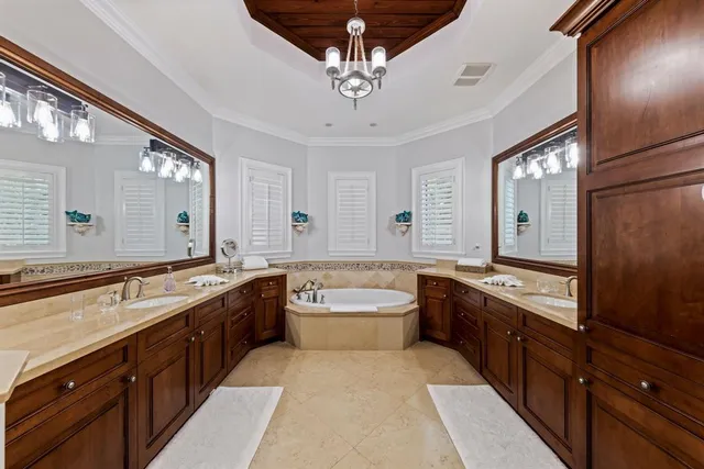 a spacious en suite bathroom with a granite countertop double vanity sink large mirror and a bathtub