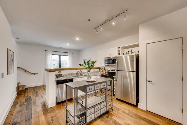 a kitchen with stainless steel appliances a refrigerator a stove a sink dishwasher and white cabinets with wooden floor