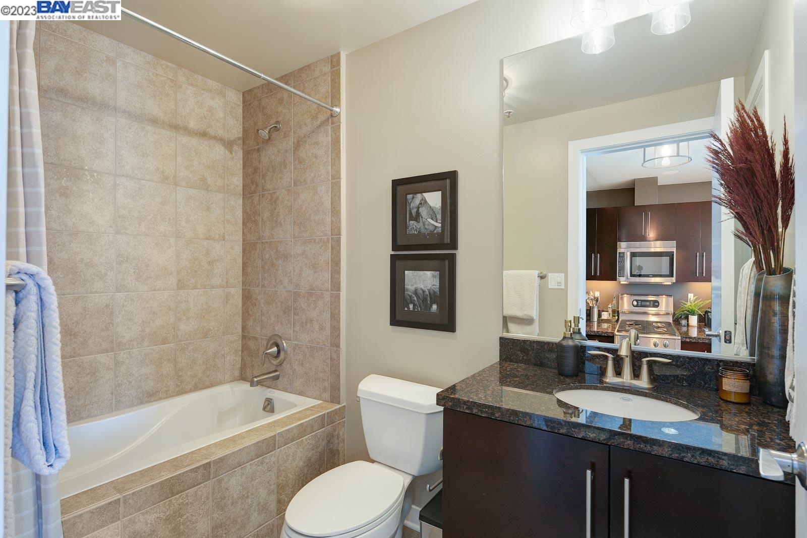 222 Broadway, Unit 1004 Oakland, CA 94607 - Photo 30 of 60 a bathroom with a granite countertop sink toilet mirror and bathtub