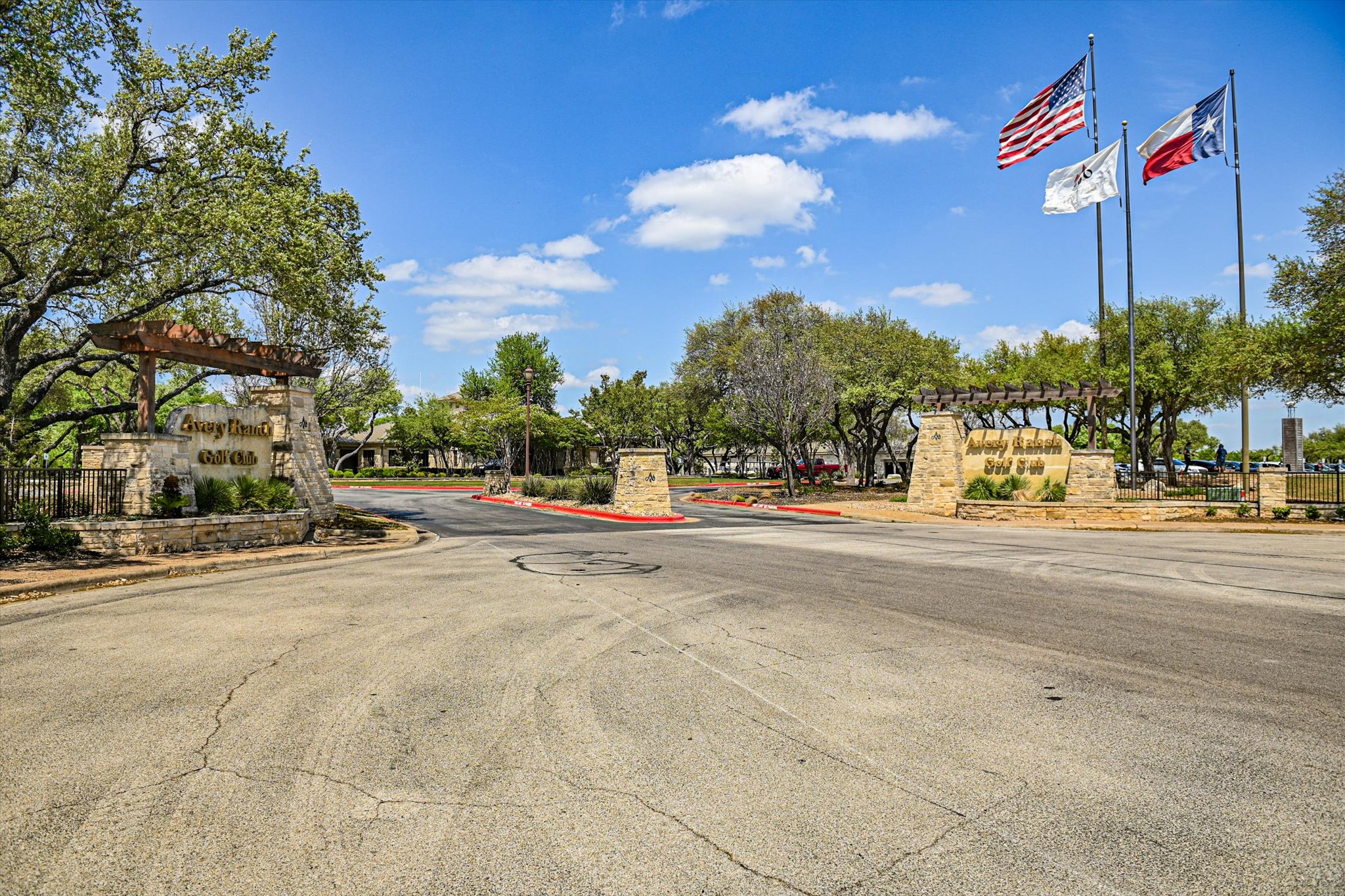 14001 Avery Ranch Boulevard, Unit 202 Austin, TX 78717 - Photo 25 of 30 Stone column entry feature with a wood pergola accent, integrated landscaping, and prominent flagpoles displaying the American and Texas flags