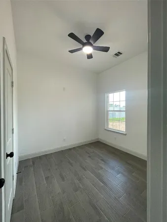 an empty room with wooden floor fan and windows
