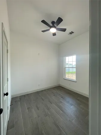 an empty room with wooden floor fan and windows
