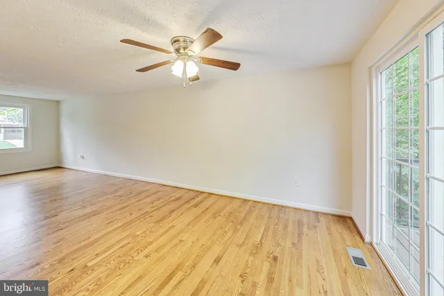 an empty room with wooden floor fan and windows