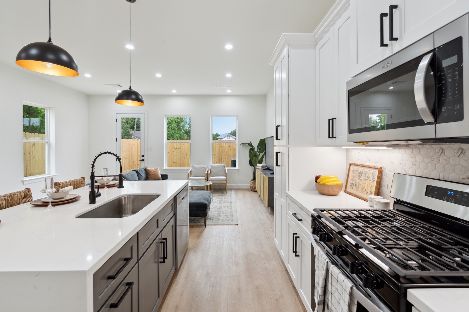 Chef's vantage point — quartz prep island with undermount sink, gas range with stainless steel microwave vent hood, and soft-close white shaker cabinetry extending into the open living zone.