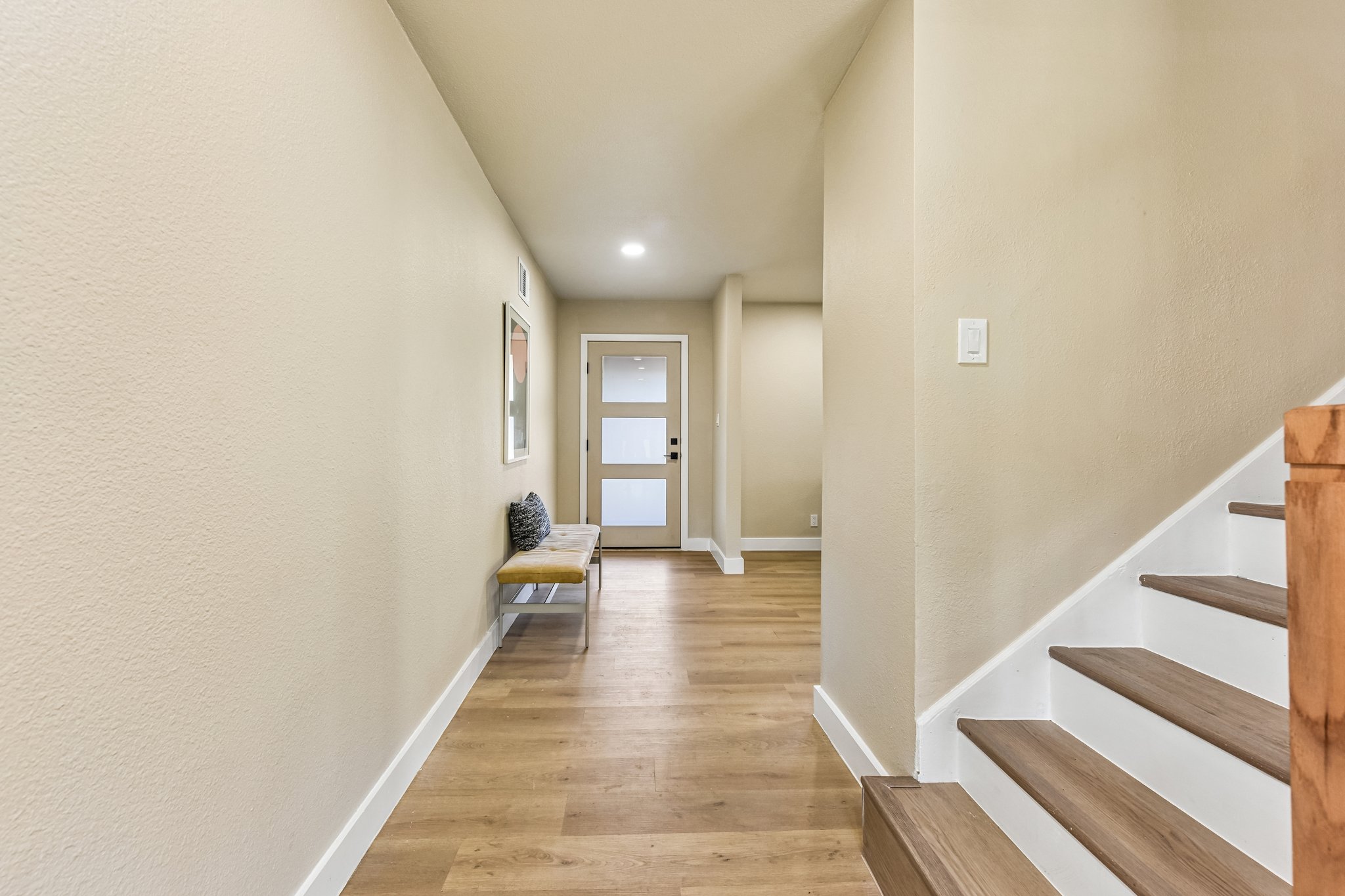7523 Glenhill Road Austin, TX 78752 - Photo 5 of 38 A welcoming entryway with warm wood floors extends to a modern glass-paneled front door, complemented by a minimalist staircase.