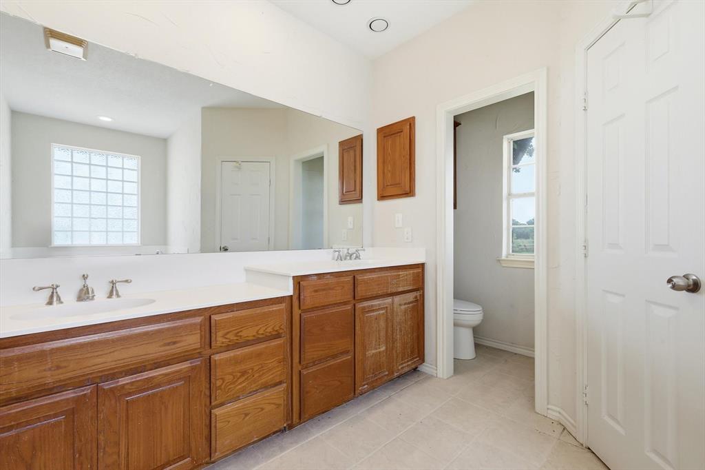12190 Bell Road Pilot Point, TX 76258 - Photo 24 of 39 Double vanity with white countertops, wood-finish cabinetry, and brushed nickel faucets