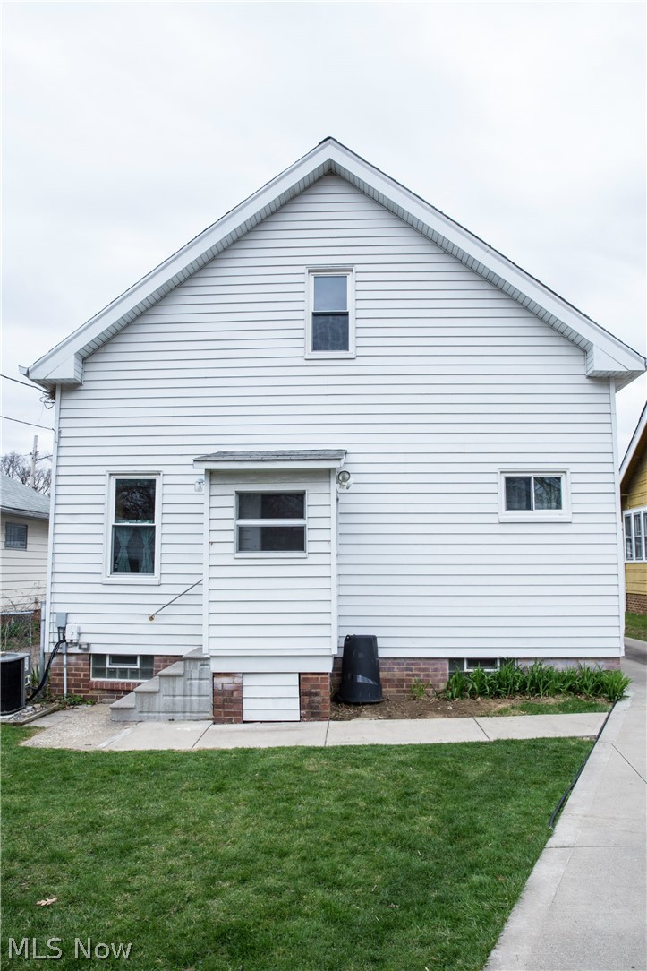 3436 Berea Road Cleveland, OH 44111 - Photo 21 of 26 Back of house with full concrete path from driveway, a view of the glass block windows in the basement, and an enclosed entrance to the house. To the left of the house is a peek at the a/c compressor.