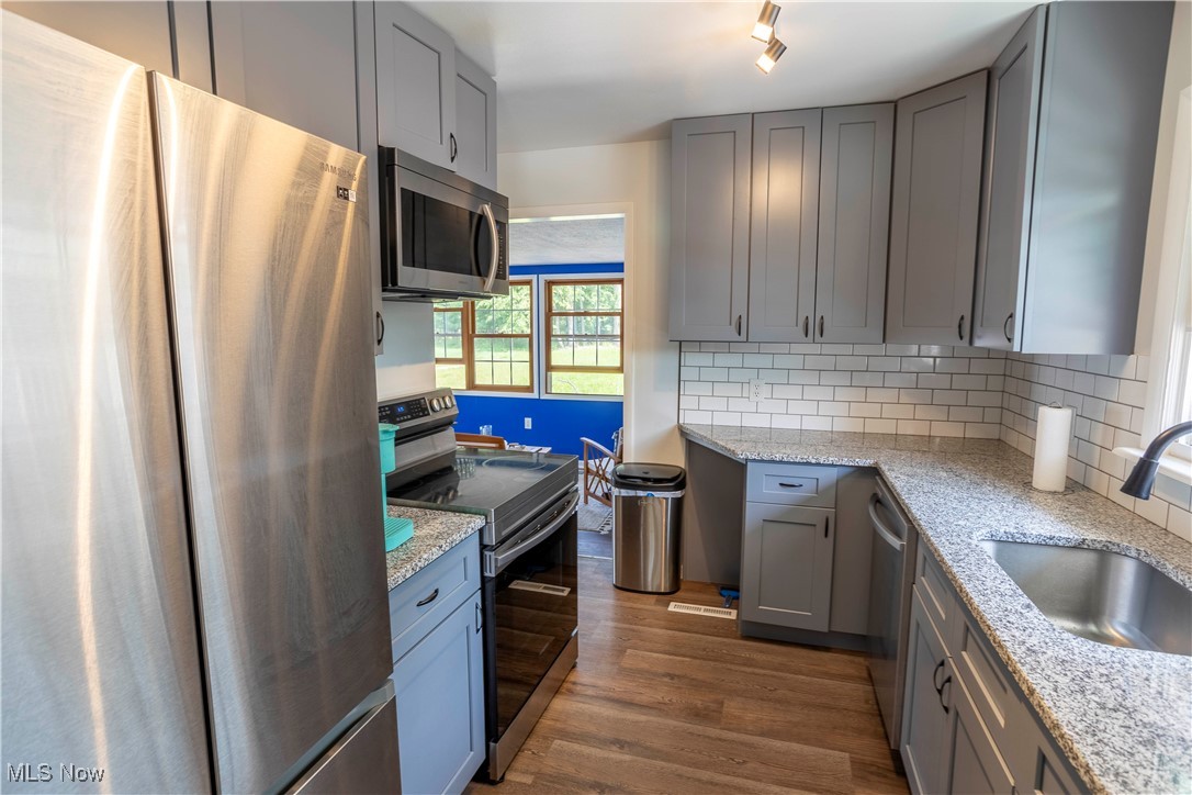 2247 Walter Road Westlake, OH 44145 - Photo 8 of 22 Kitchen with appliances with stainless steel finishes, light stone counters, dark hardwood / wood-style floors, and tasteful backsplash