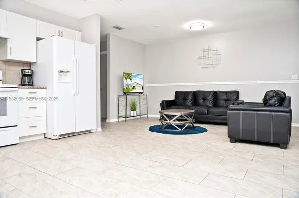 a living room with furniture a refrigerator and white cabinets