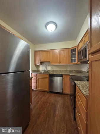 a kitchen with stainless steel appliances granite countertop a refrigerator a sink dishwasher a stove and a wooden floor