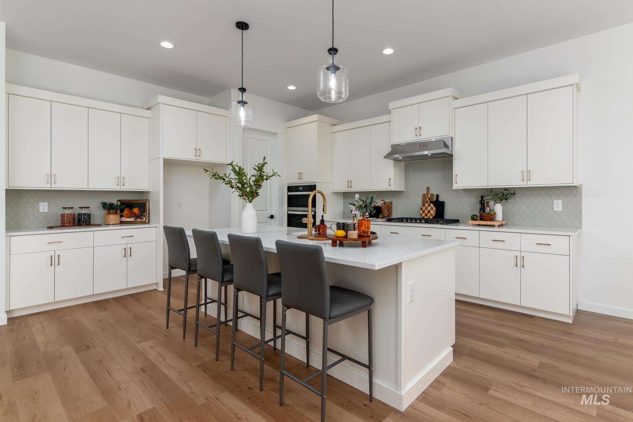 5402 Juliet Rose Avenue Caldwell, ID 83607 - Photo 5 of 20 Open-concept kitchen featuring an oversized island with seating, extensive white cabinetry, light-toned wood-finish flooring, recessed lighting, and a patterned tile backsplash