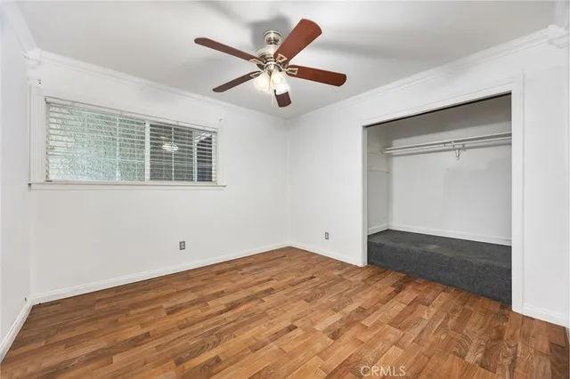 a view of an empty room with wooden floor and a ceiling fan