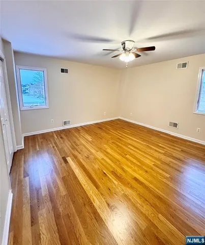 a view of an empty room with wooden floor and a ceiling fan