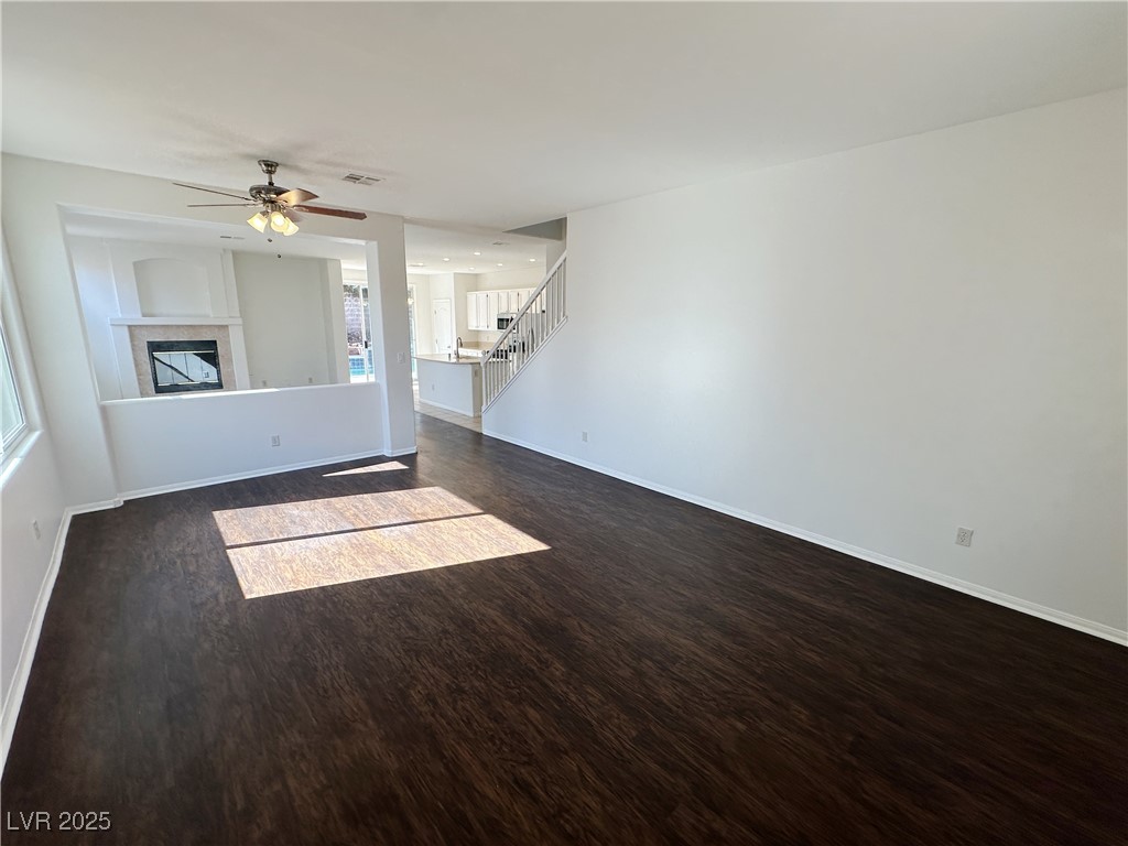 181 Ruby Ridge Avenue Henderson, NV 89002 - Photo 5 of 44 Unfurnished living room with dark wood-type flooring, a ceiling fan, a tile fireplace, and stairs