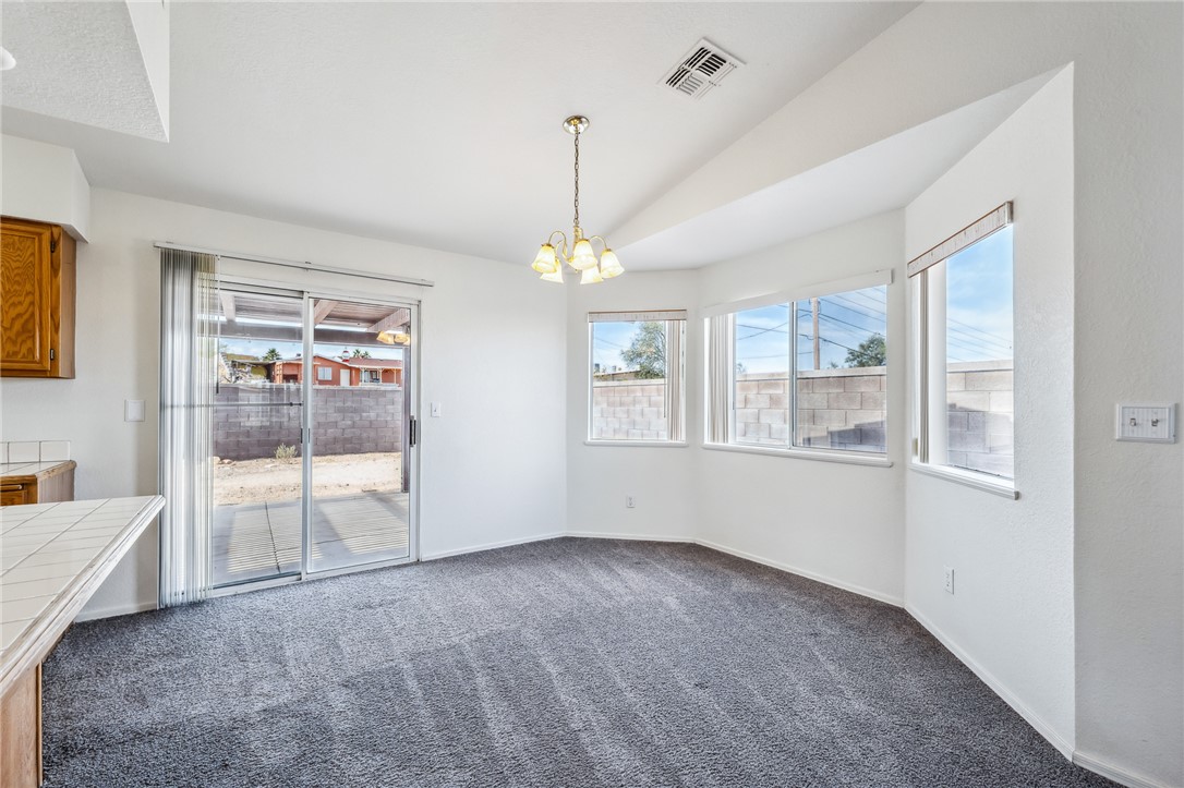 2524 South Ridge Avenue Bullhead City, AZ 86429 - Photo 16 of 64 Unfurnished dining area featuring carpet floors, vaulted ceiling, a chandelier, and baseboards
