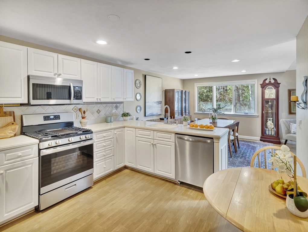 10 Kettle Lane, Unit 10 Mashpee, MA 02649 - Photo 6 of 25 a kitchen with stainless steel appliances granite countertop a stove top oven a sink dishwasher a refrigerator and a dining table with wooden floor