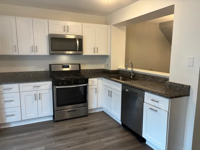 a kitchen with stainless steel appliances granite countertop a stove a sink and white cabinets